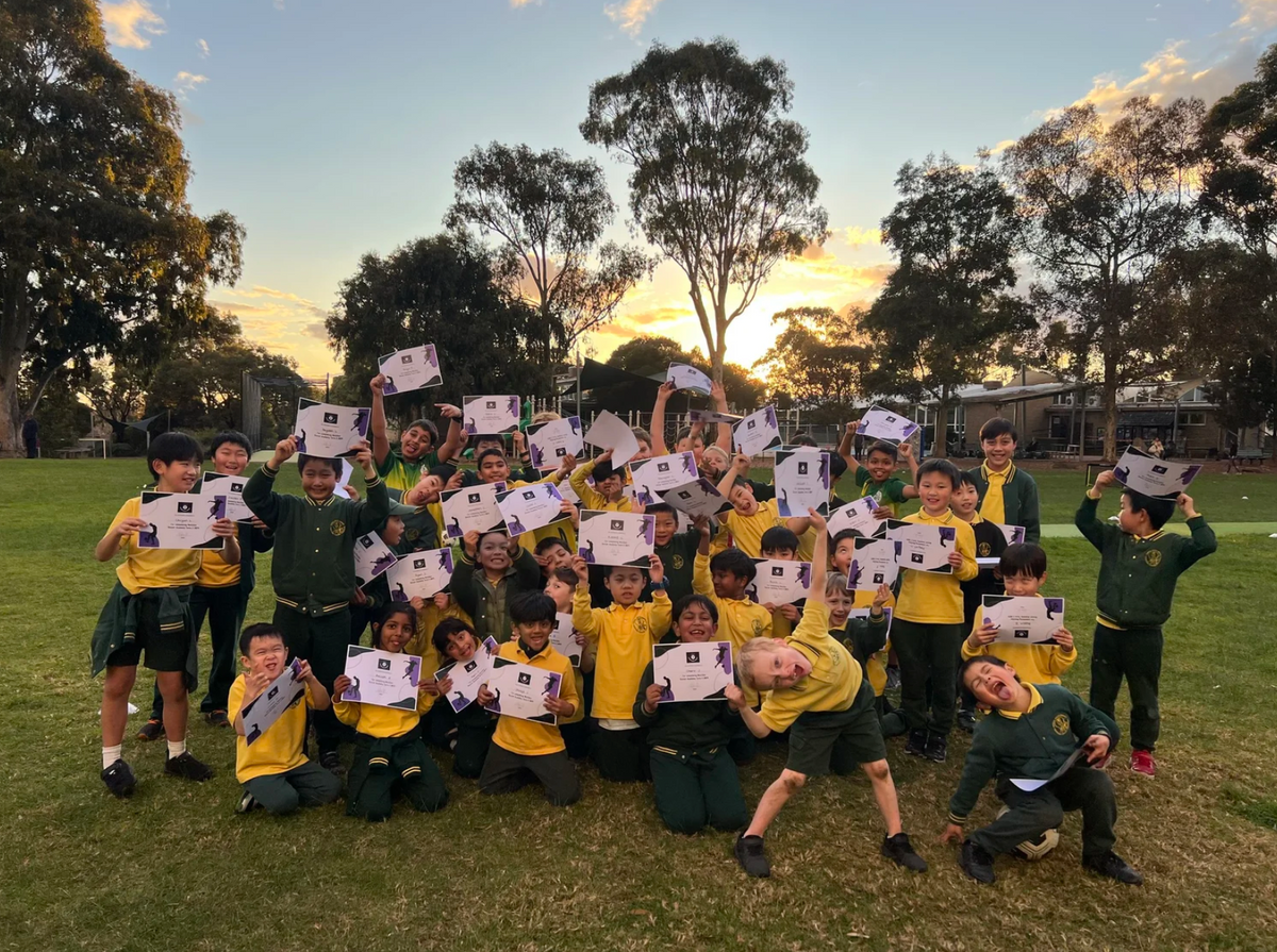Players on the school oval at sunset, holding up their end of term certificates